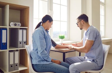 Tıbbi muayene sırasında klinikte oturan bir bayanın kan basıncını ölçen güler yüzlü genç erkek doktor terapisti. Sağlık ve Tıp Konsepti.