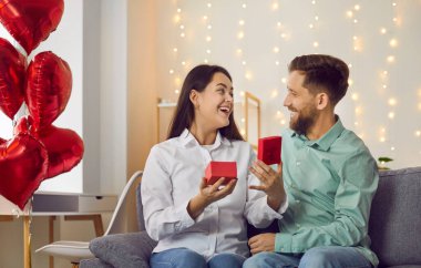 Güzel genç bir kadın Sevgililer Günü için hediye kutusunu açtığı için şaşırdı. Romantik ortamda, rahat oturma odasındaki kanepede birbirine aşık mutlu bir çift oturuyor..