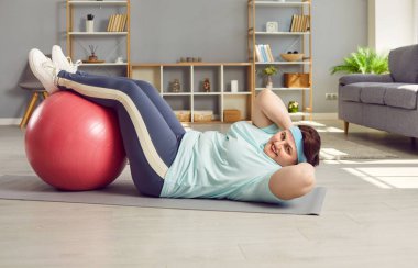 Şişman kadın evde fitbolla karın kaslarını çalıştırıyor. Artı cüsse, obez, spor giyim bölümünde spor topuyla mekik çeken şişman bir kadın. Spor, kilo kaybı, sağlıklı yaşam tarzı.