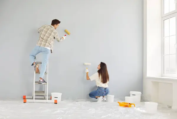 stock image Happy young married couple enjoying wall painting, enjoy home renovation fun, decorate, repair after moving into new house, excited homeowners, renters, man and woman feeling joy, working together