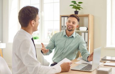 İki kişi ekip olup bir iş anlaşmasını tartışacak. İki mutlu, gülümseyen genç adam bir ofis masasında dizüstü bilgisayarla oturup, iş hakkında konuşuyor, yeni fikirler geliştiriyor ve eğleniyorlar.