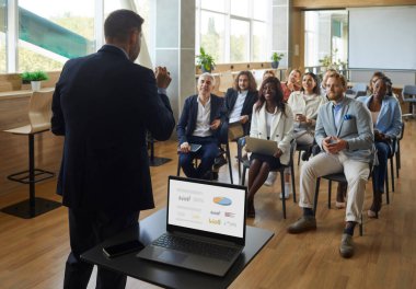 İşte öğreniyorum. İş dünyası lideri şirket brifinginde kalkınma stratejisi ve mali sonuçlardan bahsediyor. Dizüstü bilgisayardaki sunumuyla ofisteki çalışanların önünde konuşan bir iş adamı..