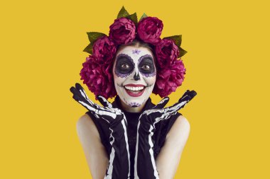 Cadılar Bayramı indirimi. Geleneksel Meksika usulü şeker kafalı güzel bir kadın Cadılar Bayramı indirimlerinden memnun. Çiçekli çelenkli mutlu kadın turuncu arka planda el ele tutuşuyor..