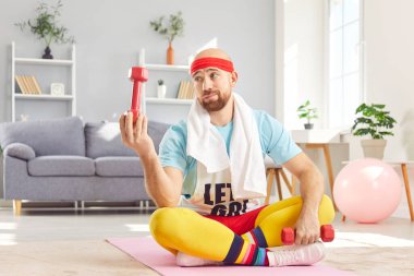 Retro spor giyim bölümündeki komik adam evde spor yapıyor, spor salonunda halter kullanıyor, yerde oturuyor. Onun hareketli spor aktivitesi jimnastik seansına mizah katıyor..