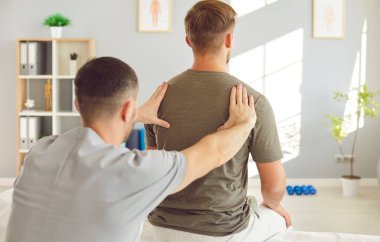 Erkek osteopat modern ofiste genç bir adamı muayene ediyor. Genç fizyoterapist rehabilitasyon kliniğinde tedavi görüyor. Kayropraktik uzmanı omurga eğriliği ve sırt ağrısı olan hastaya yardım ediyor..