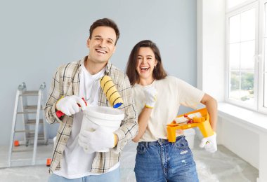 Birlikte yeni bir evi restore eden mutlu genç bir çiftin portresi. Dekorasyon ve resim yaparken neşeli ifadeleri inşaat sürecinde heyecan ve işbirliğini yansıtıyor..