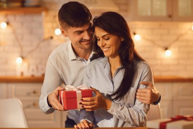 Aşık genç adam sevgilisine şefkatle sarılıyor ve Sevgililer Günü hediyesi veriyor. Mutlu çift evde kutlama yapıyor ve birlikte vakit geçiriyorlar. Aşk ve romantizm kavramı.