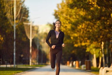 Genç bayan koşucu şehir parkında tek başına koşuyor. Sağlık, sağlık ve kardiyo için açık havada koşan sağlıklı spor yapan bir kadın. Doğada egzersiz ve sağlıklı yaşam tarzı konsepti.