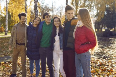 Bir grup mutlu arkadaş sonbahar parkında yürüyor. Genç beyaz insanlar, kızlar ve oğlanlar ayakta durup birbirlerine bakıyorlar ve dışarıda neşeyle gülümsüyorlar. Arkadaşlık ve birliktelik kavramı.