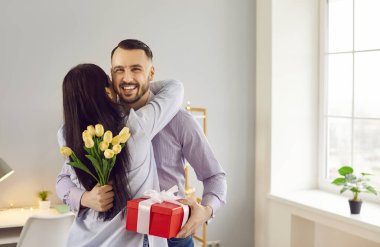 Mutlu, sevgi dolu bir kadın kocasına ya da erkek arkadaşına sarılır ve kocasına hediye olarak bir buket güzel bahar çiçeği verir. Çift, sürpriz, hediye, Sevgililer Günü, doğum günü, ilişki yıldönümü konsepti