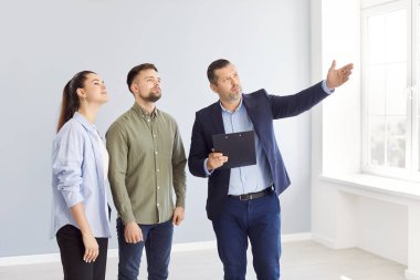 Genç ve mutlu bir çifte güzel bir ev gösteren bir emlakçı. Profesyonel emlakçı parlak yeni bir daire gösterdi. Başarılı bir aile ev sahibi olmaya hazır. Emlak piyasası kavramı.