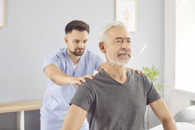 Rehabilitasyon doktoru yaşlı bir adamın omuzlarını düzeltir, yakın plan. Rehabilitasyon merkezinde profesyonel tıbbi müdahale. Konsept tıbbi hizmetler, fizyoterapi