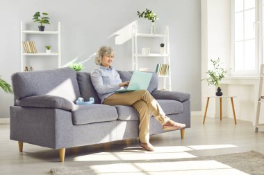 Evdeki kanepede oturan mutlu son sınıf öğrencisi dizüstü bilgisayarla online eğlenceye dalmış. Gülümseme, teknolojinin olumlu etkisini sergileyerek, internet eğlence faaliyetlerindeki keyfi yansıtır..