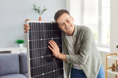 Mutlu gülümseyen genç bir adamın portresi evde güneş paneli satın aldı. Ev için sürdürülebilir fotovoltaik enerji çözümleri. Alternatif enerji, tasarruf kaynakları ve sürdürülebilir yaşam tarzı kavramı