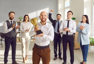 Ofis ödülü kazanmak, erkek çalışanları ödüllendirmek için iş ödülü. İş yeri yarışmasının galibi, mutlu iş adamı zafer kupası tutuyor, dost canlısı iş arkadaşları tebrik ediyor