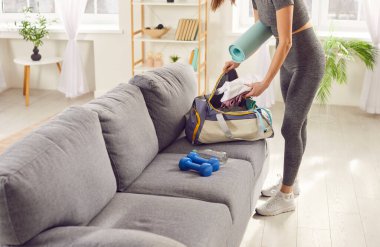 Sporcu kadın spor çantasını evde spor antrenmanı için hazırlıyor. Genç kız oturma odasında aktif gün için spor eşyaları topluyor. Sağlık ve sağlıklı yaşam tarzı kavramı.