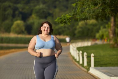 Yaz parkında koşuşturan şişman ve mutlu bir kadının portresi. Ayrıca spor giysili bir kız dışarıda koşuyor. Kilo kaybı, vücut pozitifliği, spor ve spor yaşam tarzı konsepti.