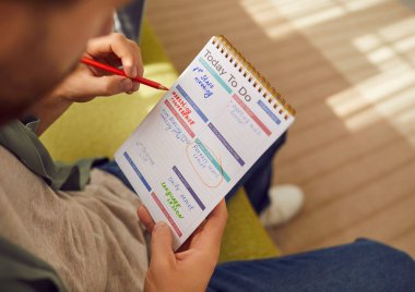 Not defterinde yazmakla meşgul bir adam. Elinde kalem ve üretkenlik planlayıcısı olan bir adam, iş görevlerini ve sorumluluklarını sayfa üzerine not ediyor ve tasarım şablonlarını hazırlıyor. Yakın çekim, yakın çekim.
