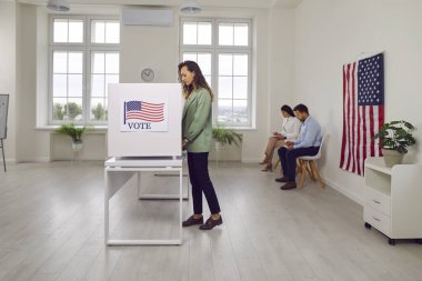 Seçim günü oy verme merkezinde oy kullanan Amerikalı bir kadın var. İkonik Amerikan bayrağı, vatandaşlık mücadelesi ve ABD 'ye demokratik katılımın önemini vurguladı.