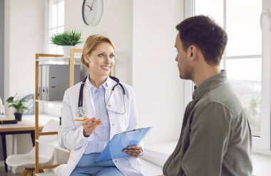 Mutlu genç doktor, kadın pratisyen doktor erkek hastaya sağlık testi sonuçlarını gösteriyor, sağlık sigortası anlaşmasını tartışıyorlar, klinikte hastalık geçmişini analiz ediyorlar, klinikte konuşuyorlar.