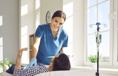 Genç bayan hemşire ya da doktor randevu ile rapor tutuyor ve klinikte kanepede yatan erkek hastasına danışmanlık yapıyor ve serum ve vitamin tedavisi görüyor..
