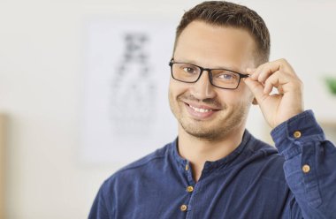 Gözlük denerken gülümseyen mutlu bir adamın portresi. Onun olumlu ifadesi görme bakımının önemini ve optik sağlık için doğru gözlüğü bulmanın sevincini vurgular..