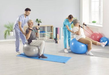 Hemşire ya da sağlık çalışanları üst düzey hastalara lastik bant ile spor esneme egzersizleri yapmaları ve rehabilitasyon kliniğinde topa iyi bakmaları için yardım ediyor. Fizyoterapist yaşlı bir adama ve kadına rehabilitasyonda yardım ediyor..