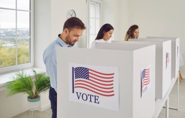 Amerika 'da seçimler. Seçimler sırasında oy kullanma kabinlerinde oy kullanan farklı düşünceli insanlar. Seçim günü üzerinde Amerikan bayrağı olan üç kişi oy kabininde duruyor. Yan görünüm.