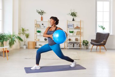 Mutlu enerjik Afro-Amerikan kadın evde antrenman yapıyor. Neşeli, neşeli, gülümseyen genç, çekici bayan atlet oturma odasının iç kısmında spor egzersizleri yapıyor.