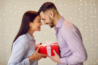 Aşık genç bir çiftin portresi elinde kırmızı hediye kutusu olan bir kadın ve erkek. Arka plandaki ışıklarda durdukları için birbirlerini tebrik ediyorlar. Sevgililer Günü konsepti.