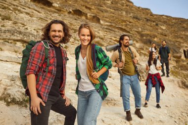 Tatil gezisi sırasında dağlarda bir grup arkadaşla çevrili bir çift portresi. Yürüyüş takımı dağ zemininde bir topluluk oluşturduğu için atmosfer gözle görülür..