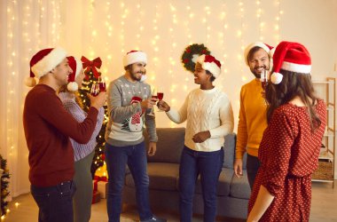 Yeni 2022 yılı yaklaşıyor. Bir grup neşeli, çok ırklı genç arkadaş yeni yılı sıcak ev ortamında kutluyor. Noel Baba şapkalı insanlar yeni yıl partisinde tost ve kadeh tokuşturarak kırmızı şarap içiyorlar..