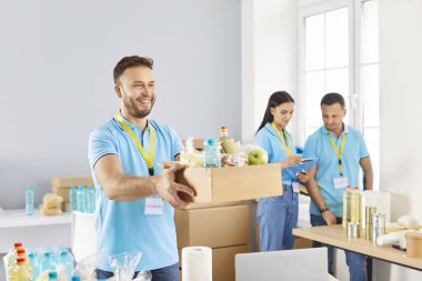 İnsani yardım merkezinde çalışırken bir kutu yiyecek taşıyan gülen bir gönüllü. Bağış hizmetlerini desteklemek ve yardım sağlamak için yaptığı hayır işleri..