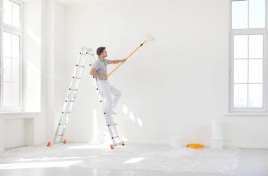 Erkek ressam ya da inşaat işçisi duvar yüzeyini boya fırçasıyla beyaz renge boyuyor, merdiven üstündeki tamirci, oda, bina onarımı, iç mimari ve tasarım işlerini bitiriyor. 