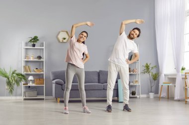 Genç, gülümseyen mutlu çift evdeki oturma odasında spor egzersizi yapıyor. Spor giyimli neşeli erkek ve kadın içeride spor yapıyor. Fitness ve sağlıklı yaşam tarzı konsepti.
