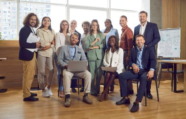 Bir grup iş adamı, kadın ve erkek kameraya bakıyor ve içeride gülümsüyor. Şirket çalışanları ya da bir grup personel güvenle ofiste duruyor. İş adamları portresi.