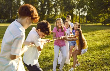 Bir grup mutlu, güler yüzlü çocuk yaz tatillerinde halatla parkta oynuyorlar. Neşeli okul çocukları kamptaki yeşil çimlerde eğleniyorlar..