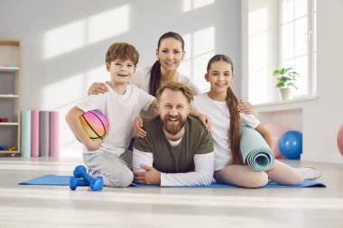 Çocuklar spor salonunda ellerinde spor malzemeleriyle yoga minderinde oturup antrenmandan sonra neşeli bir şekilde kameraya bakarken mutlu ve sportif bir aile. Spor sporu ve sağlıklı yaşam tarzı konsepti.