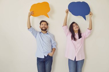 Renkli konuşma baloncukları ya da bulutlar tutan ve gri arka planda gülümseyen mutlu iki meslektaşız. Fikir ve görüşlerini paylaşıyorlar, mutlu ve işbirlikçi takım dinamiğini yansıtıyorlar..