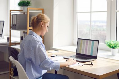 Ofiste dizüstü bilgisayar ve belgelerle çalışan bir kadın, muhasebe ve mali denetim işlerini yürütüyor. Finansal görevlere, şirket için çevrimiçi kayıtlara ve belgelere odaklanmış durumda..