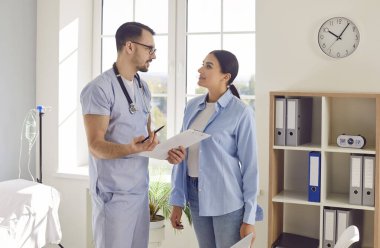 Erkek doktor ya da hemşire, hastane ofisindeki kadın hastaya uzman tıbbi danışmanlık ve sağlık tavsiyeleri sunmak için işbirliği yaparak, kişisel ve özenli bakım.