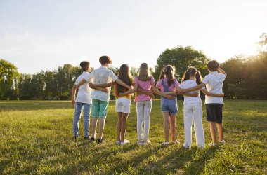 Çocuklar yazın parkta birbirlerine sokuluyorlar. Arkadaşlar doğada birlikte oynuyorlar. Grubun arkasındaki çocuklar sabah çimlerin üzerinde durup gökyüzündeki yeşil ağaçların üzerinden güneşin doğuşunu izliyorlar.