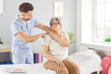 Genç erkek fizyoterapist, kayropraktik uzmanı ya da osteopat, omurga problemleri olan yaşlı kadınlara yardım eder. Klinikte rehabilitasyon sırasında sırtı ya da boynu ağrıyan eski bir hastayla manuel terapi uzmanı..