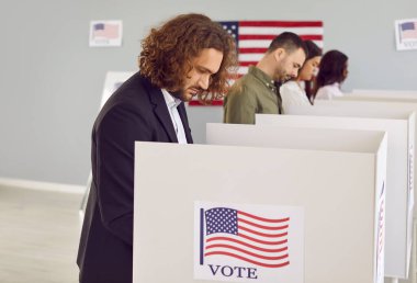 Seçim günü oy veren ve sandığa oy veren genç bir Amerikalı 'nın yan görünüm portresi. Çeşitli Amerikan vatandaşları oy kabininde duruyor..