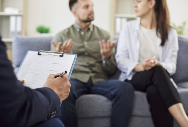 Genç evli çift, erkek psikologla aile terapisi sırasında danışmanlık koltuğunda oturup çözüm bulmaya çalışıyor. Etkili evlilik terapisi konsepti.