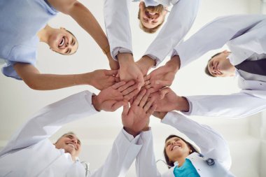 Beyaz üniformalı doktorların hastane ya da klinikte daireler çizip kollarını yığının içine koymaları. Tıbbî personel yığını. Birlik, ortaklık, takım çalışması ve sağlık hizmetleri kavramı