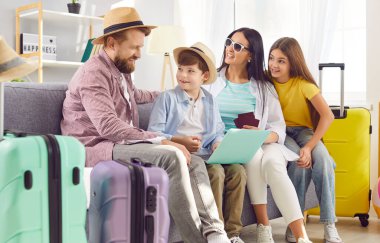 Dört kişilik mutlu bir aile, çocuklar internet üzerinden bilet alıyor ve dizüstü bilgisayarlarıyla yaz tatilini planlayan bavullarıyla oturma odasındaki koltukta oturuyor. Tatil gezisi konsepti.