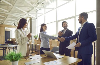 İş adamları ofiste buluşur, başarılı bir anlaşma yapar ve el sıkışırlar. Mutlu kadın ve erkek gülümser ve meslektaşları el çırparken el sıkışırlar. Takım çalışması, profesyonel ortaklık kavramı