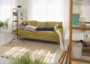 Adam evde damar içi vitamin tedavisi görüyor. Kolunda serum iğnesiyle oturma odasındaki kanepede yatan mutlu ve rahat bir adam. Vitamin terapisi konsepti