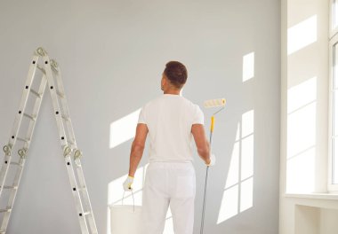 Profesyonel bir ressam, bir apartman dairesinde elinde tekerlekli fırça ve kovayla duruyor. Uzmanlığı duvarları değiştiriyor, eve inşaat sanatını getiriyor..